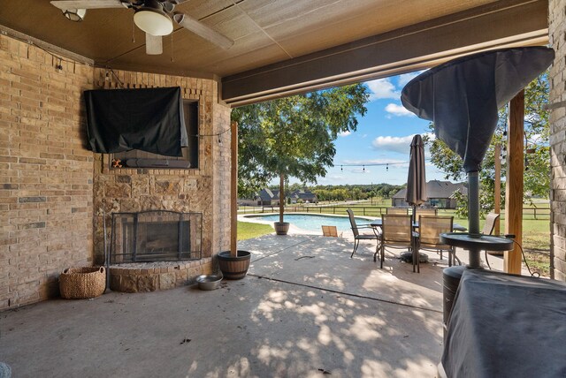 view of patio with a fenced in pool, ceiling fan, and an outdoor stone fireplace