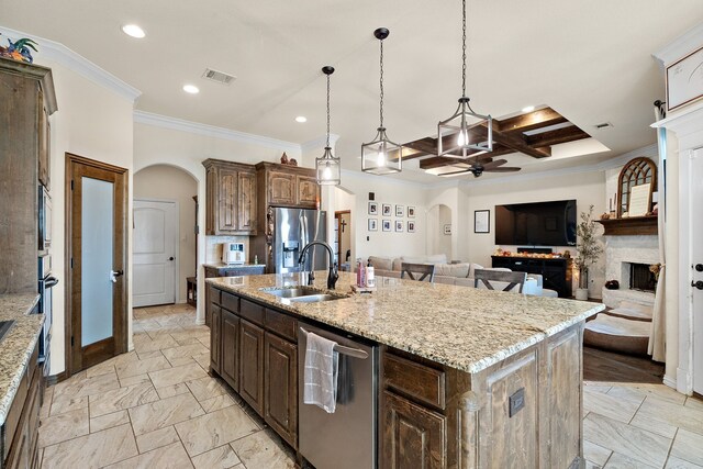 kitchen featuring sink, a large fireplace, decorative light fixtures, an island with sink, and coffered ceiling