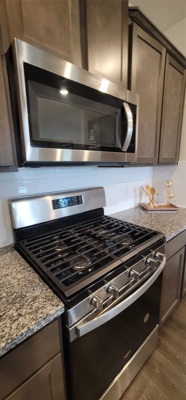 kitchen featuring dark hardwood / wood-style floors, stainless steel appliances, dark brown cabinetry, light stone counters, and tasteful backsplash