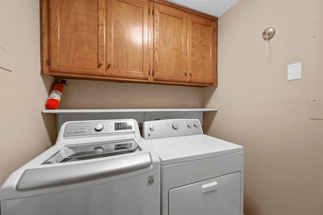 laundry room featuring washer and clothes dryer, a textured ceiling, and cabinets