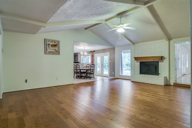 unfurnished living room featuring vaulted ceiling with beams, ceiling fan with notable chandelier, a textured ceiling, a brick fireplace, and hardwood / wood-style floors