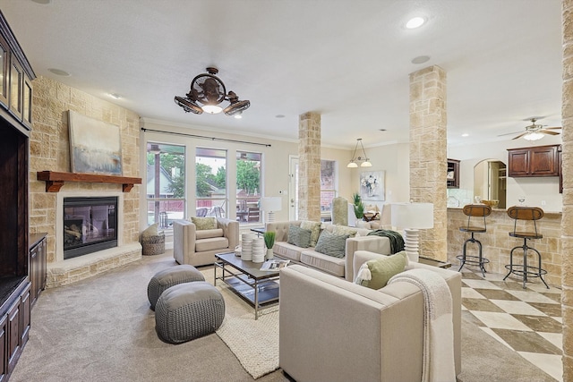 living room with crown molding, ornate columns, a stone fireplace, and ceiling fan