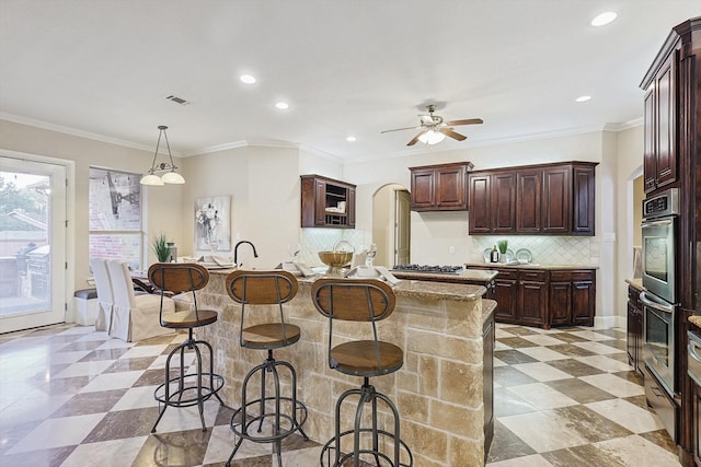 kitchen with crown molding, ceiling fan, a center island with sink, and backsplash