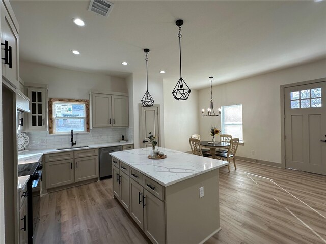 kitchen featuring light stone counters, stainless steel dishwasher, decorative light fixtures, a kitchen island, and light wood-type flooring