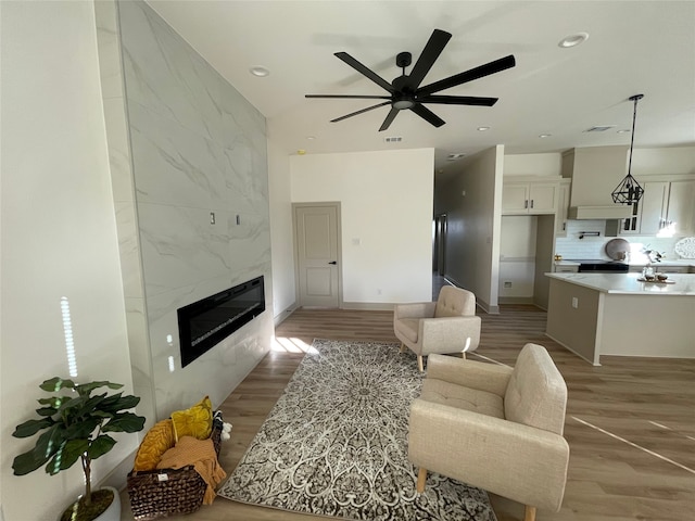 living room with a high end fireplace, light wood-type flooring, and ceiling fan