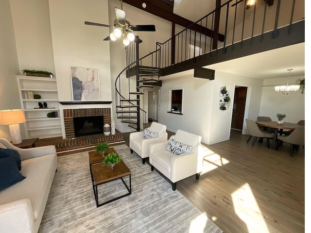 living room featuring ceiling fan with notable chandelier, wood-type flooring, a high ceiling, and a brick fireplace