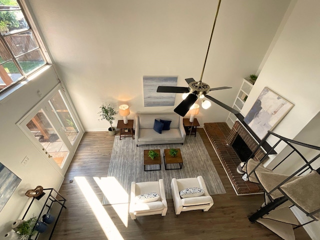 living room featuring ceiling fan, dark hardwood / wood-style flooring, a towering ceiling, and a brick fireplace