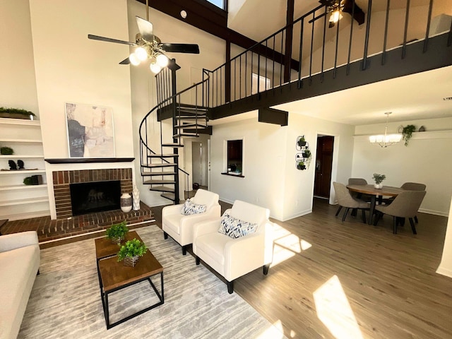 living room featuring hardwood / wood-style flooring, a high ceiling, ceiling fan with notable chandelier, and a brick fireplace