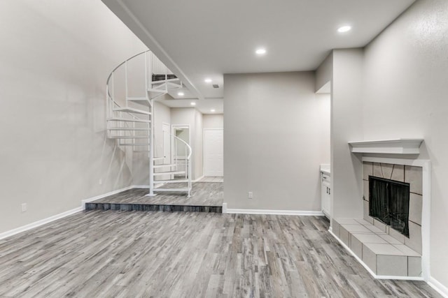 unfurnished living room with light wood-type flooring and a tiled fireplace