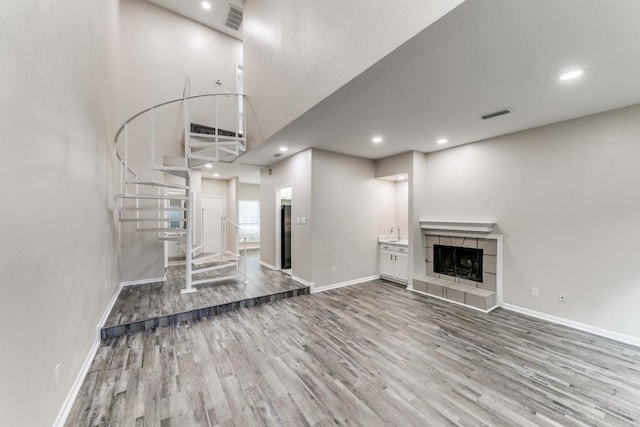 unfurnished living room with wood-type flooring, sink, a towering ceiling, and a tiled fireplace