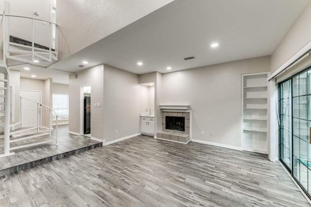 unfurnished living room featuring a fireplace, plenty of natural light, built in shelves, and light hardwood / wood-style flooring