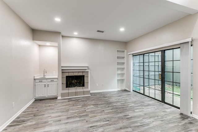 unfurnished living room featuring a tile fireplace, built in shelves, and light hardwood / wood-style floors