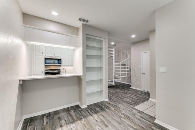 kitchen with stove, wood-type flooring, kitchen peninsula, and white cabinets