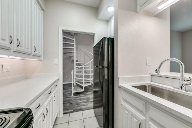 kitchen featuring white cabinetry, sink, range with electric stovetop, black refrigerator, and light tile patterned floors