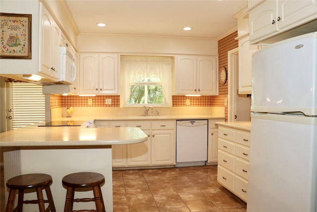 kitchen with a breakfast bar, ornamental molding, white cabinets, and white appliances