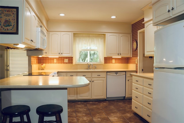 kitchen with white appliances, sink, white cabinetry, ornamental molding, and a breakfast bar