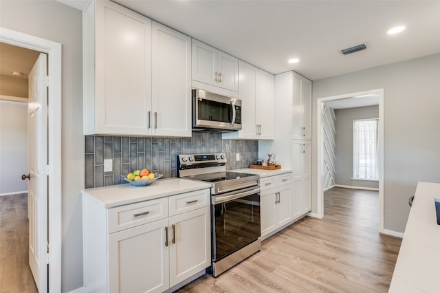 kitchen with backsplash, appliances with stainless steel finishes, light hardwood / wood-style flooring, and white cabinetry