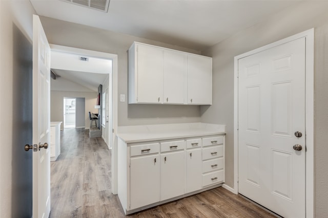 kitchen featuring vaulted ceiling, white cabinets, and light wood-type flooring