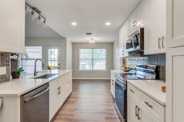 kitchen featuring appliances with stainless steel finishes, sink, light wood-type flooring, backsplash, and white cabinetry