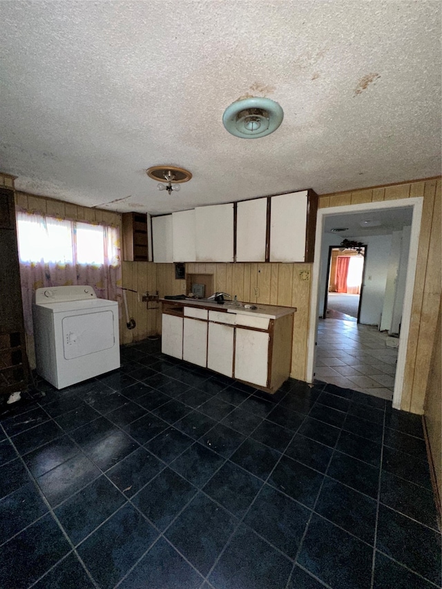 kitchen with washer / dryer, white cabinetry, a textured ceiling, and wooden walls