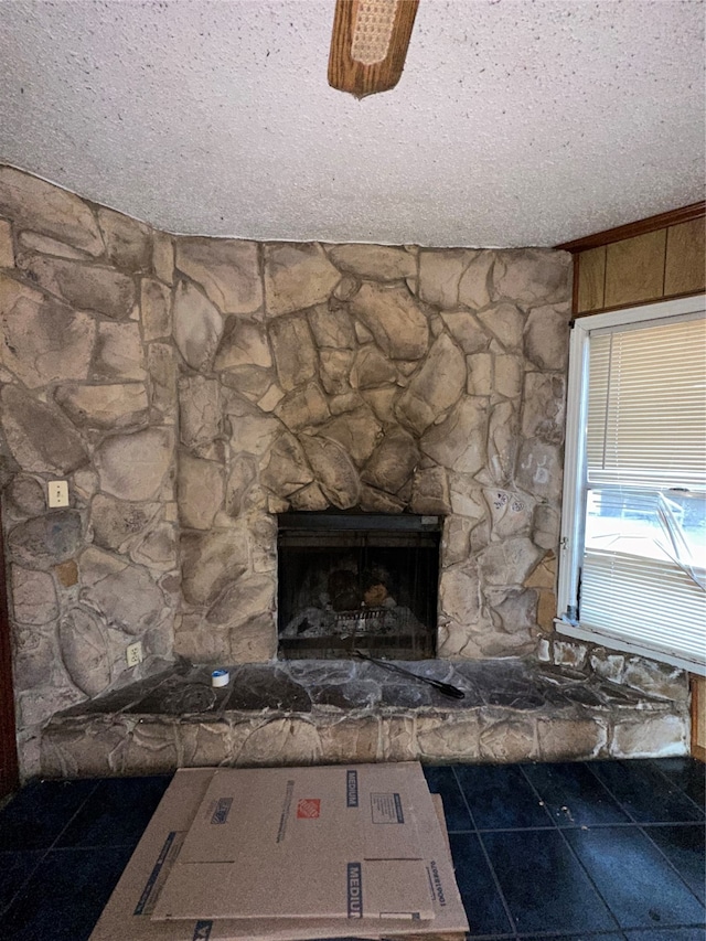 interior details featuring a stone fireplace, a textured ceiling, tile patterned floors, and ceiling fan