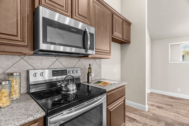 kitchen featuring backsplash, appliances with stainless steel finishes, light stone countertops, and light wood-type flooring