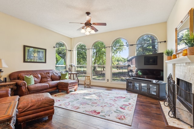 living room featuring a textured ceiling, a healthy amount of sunlight, a tiled fireplace, and dark hardwood / wood-style flooring