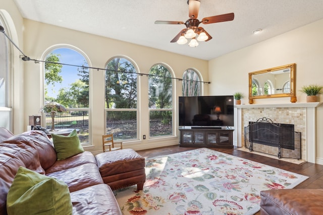 living room with a tiled fireplace, a textured ceiling, dark hardwood / wood-style floors, and ceiling fan