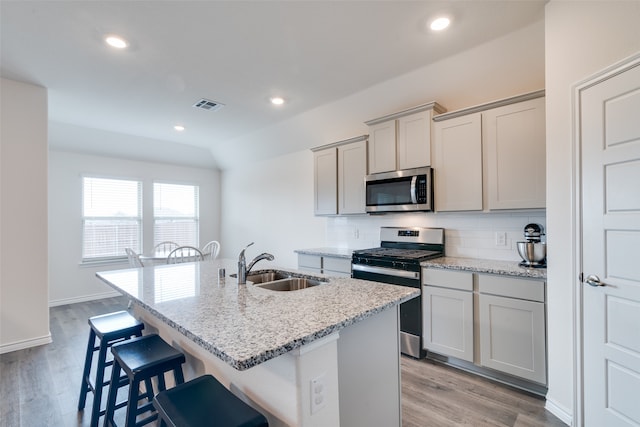 kitchen with stainless steel appliances, a center island with sink, sink, gray cabinets, and light hardwood / wood-style floors