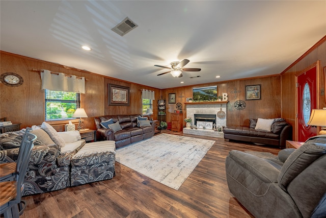 living room featuring ceiling fan, a brick fireplace, dark wood-type flooring, crown molding, and wooden walls