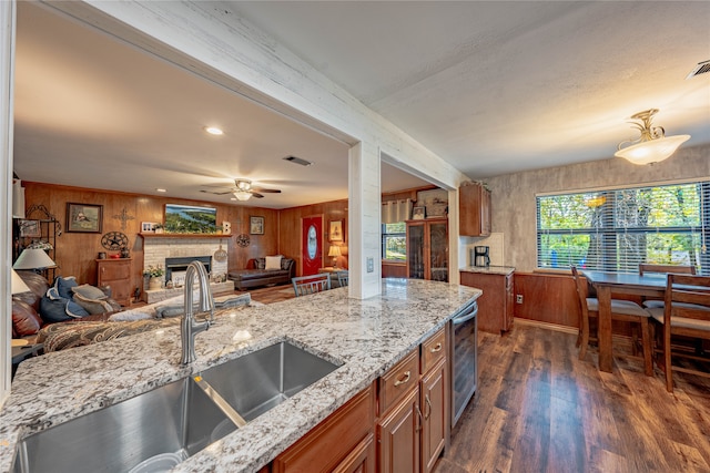 kitchen featuring dark hardwood / wood-style floors, wooden walls, sink, and a brick fireplace