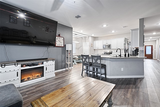 kitchen featuring appliances with stainless steel finishes, stone countertops, dark hardwood / wood-style flooring, a kitchen breakfast bar, and white cabinets