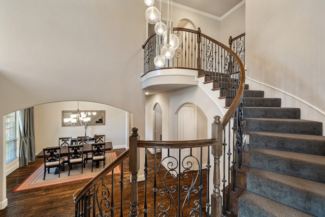 stairway with hardwood / wood-style floors, a high ceiling, crown molding, and a notable chandelier