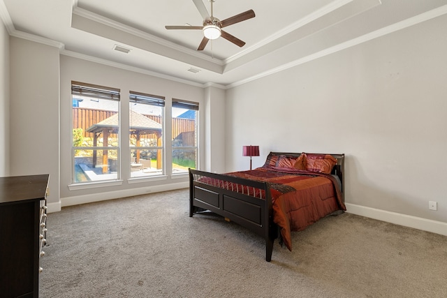 carpeted bedroom with ceiling fan, crown molding, and a tray ceiling