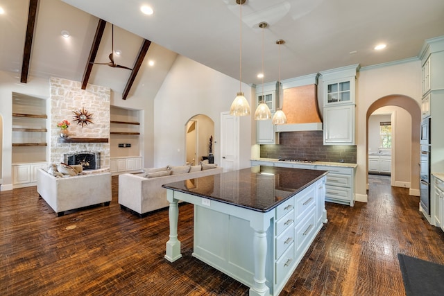 kitchen featuring custom range hood, decorative light fixtures, a stone fireplace, a kitchen island, and white cabinets