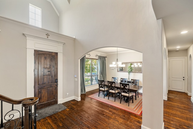 foyer with a towering ceiling, a notable chandelier, dark hardwood / wood-style floors, and crown molding