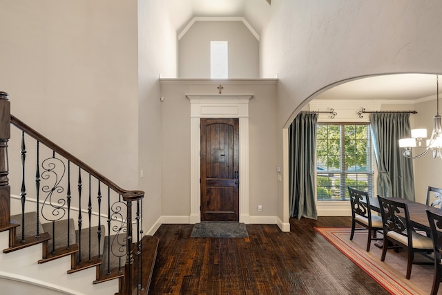 entryway featuring dark wood-type flooring, high vaulted ceiling, crown molding, and a notable chandelier