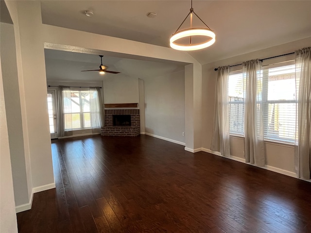 unfurnished living room featuring dark hardwood / wood-style flooring, lofted ceiling, a brick fireplace, and ceiling fan