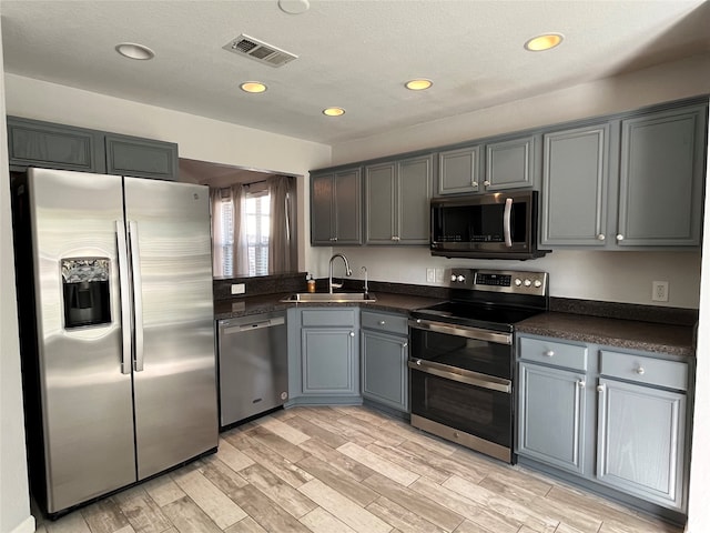 kitchen featuring appliances with stainless steel finishes, a textured ceiling, light wood-type flooring, gray cabinetry, and sink