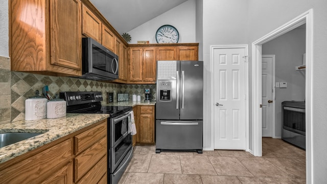 kitchen with light stone countertops, appliances with stainless steel finishes, vaulted ceiling, and decorative backsplash