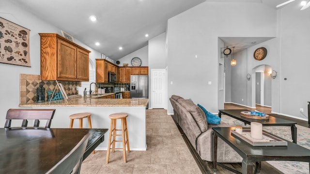 kitchen featuring decorative backsplash, a kitchen breakfast bar, sink, appliances with stainless steel finishes, and high vaulted ceiling