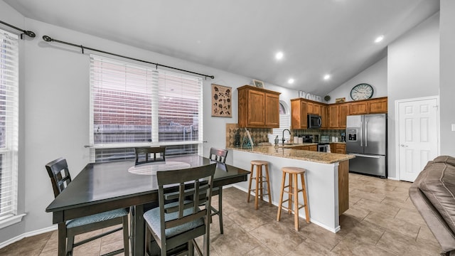 kitchen with kitchen peninsula, decorative backsplash, light stone countertops, sink, and stainless steel appliances