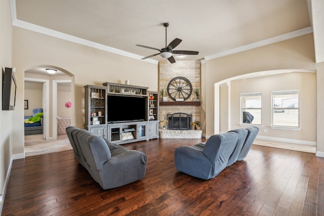 living room featuring a stone fireplace, ornamental molding, dark wood-type flooring, and ceiling fan