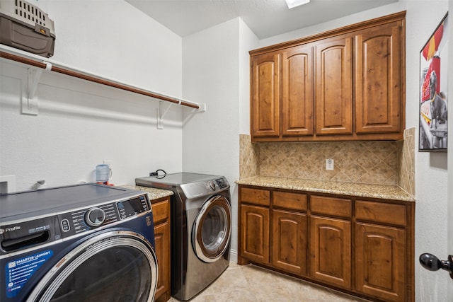 washroom featuring washing machine and dryer, light tile patterned flooring, and cabinets