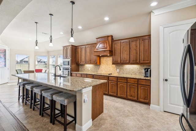 kitchen featuring light stone countertops, a kitchen breakfast bar, hanging light fixtures, decorative backsplash, and a center island with sink