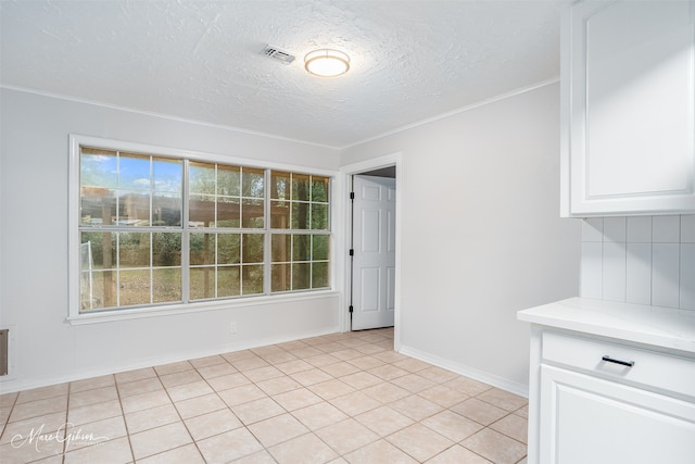 unfurnished dining area with light tile patterned flooring, a textured ceiling, and ornamental molding