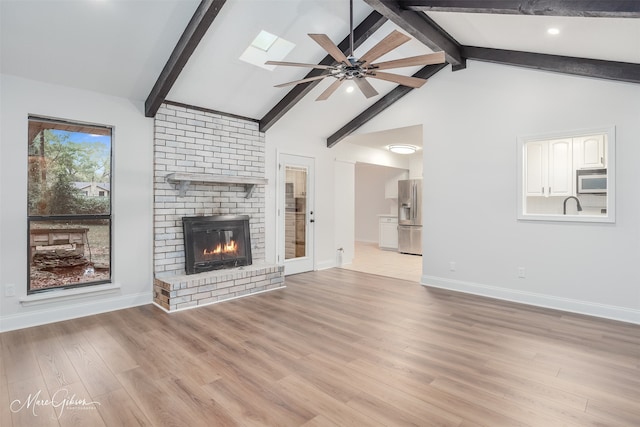 unfurnished living room featuring a brick fireplace, lofted ceiling with skylight, ceiling fan, and light wood-type flooring