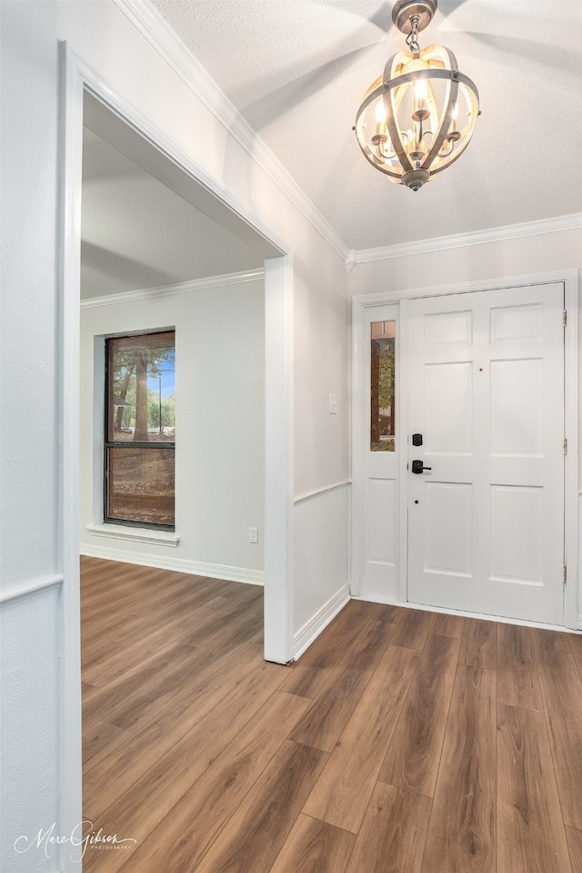 entryway with a textured ceiling, an inviting chandelier, dark wood-type flooring, and crown molding