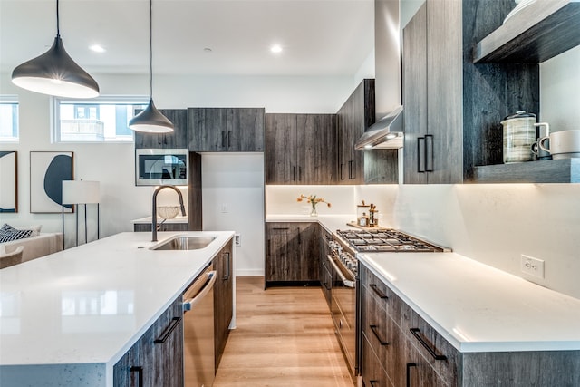 kitchen with stainless steel appliances, a center island with sink, sink, decorative light fixtures, and light wood-type flooring