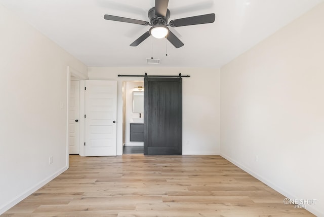 spare room featuring light hardwood / wood-style flooring, a barn door, and ceiling fan